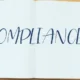 compliance o que é: Cartaz escrito "Compliance" com pessoas trabalhando em volta